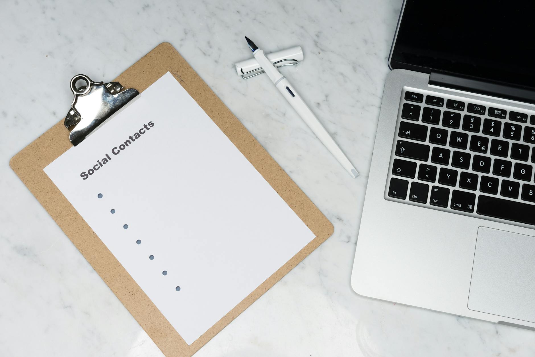 Minimalist workspace featuring a clipboard, laptop, and pen on a marble surface.