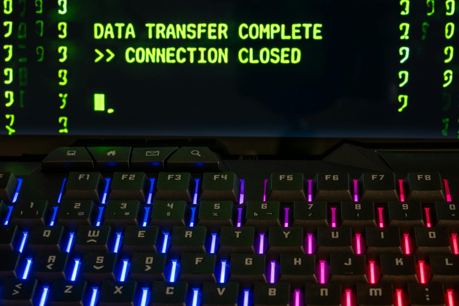Close-up of a RGB lit keyboard with a screen displaying 'Data Transfer Complete'.