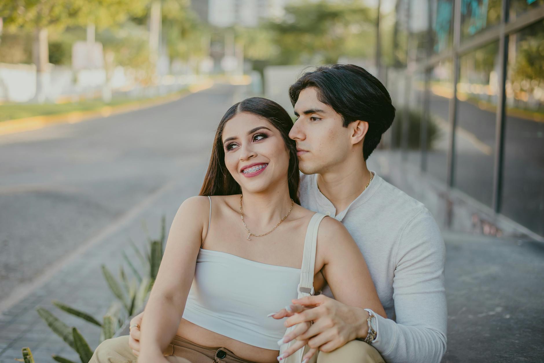 Happy couple sitting together on a city sidewalk, smiling with affection.