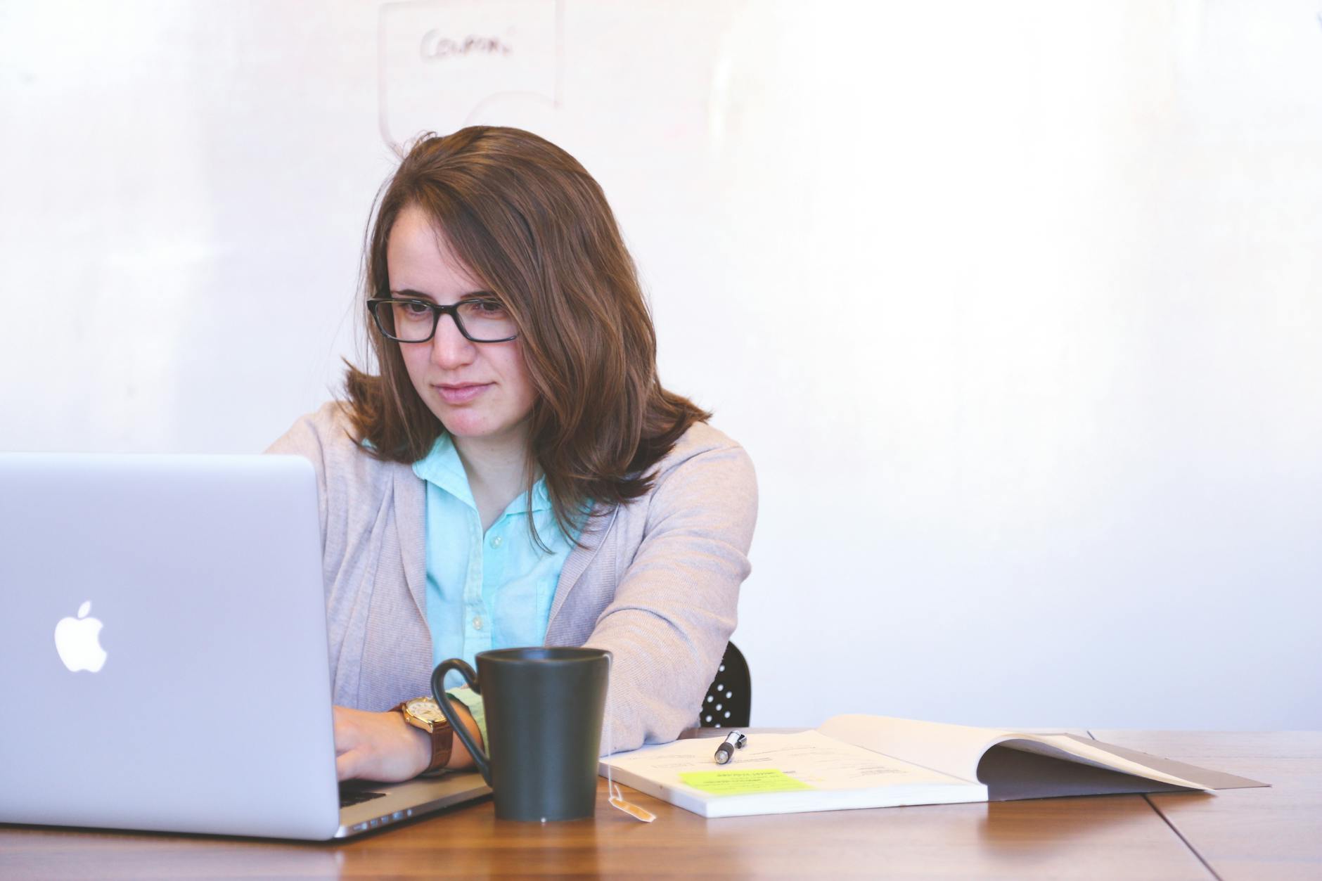 Focused businesswoman using a laptop at a desk with a mug and open notebook.