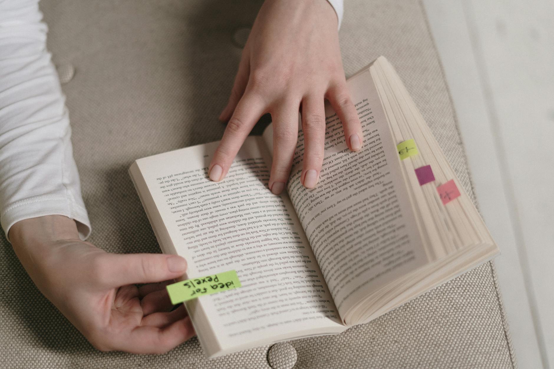 An up-close view of hands holding an open book with colorful bookmarks, ideal for literary themes.
