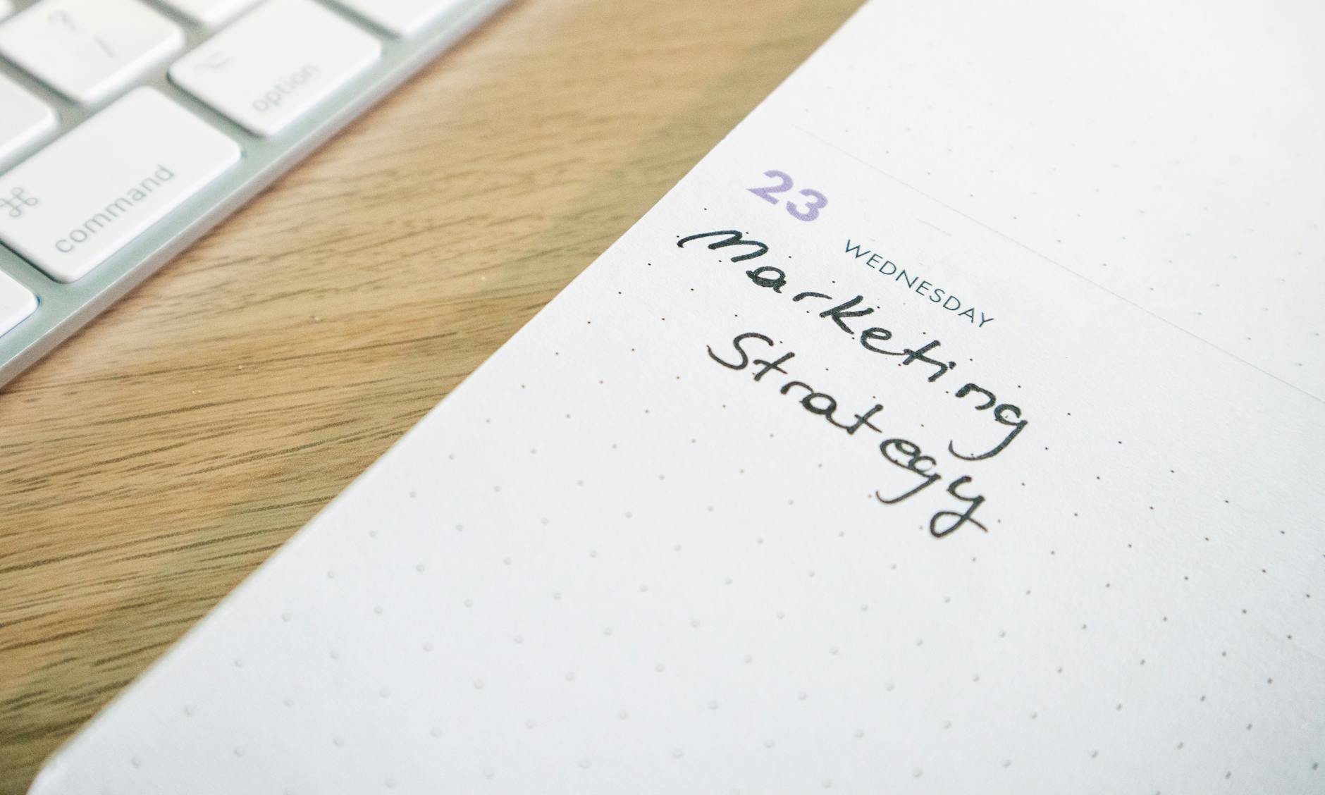 Close-up of a planner with 'Marketing Strategy' handwritten alongside keyboard.
